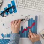 top-view-office-desk-with-growth-chart-hands-holding-magnifying-glass (1)